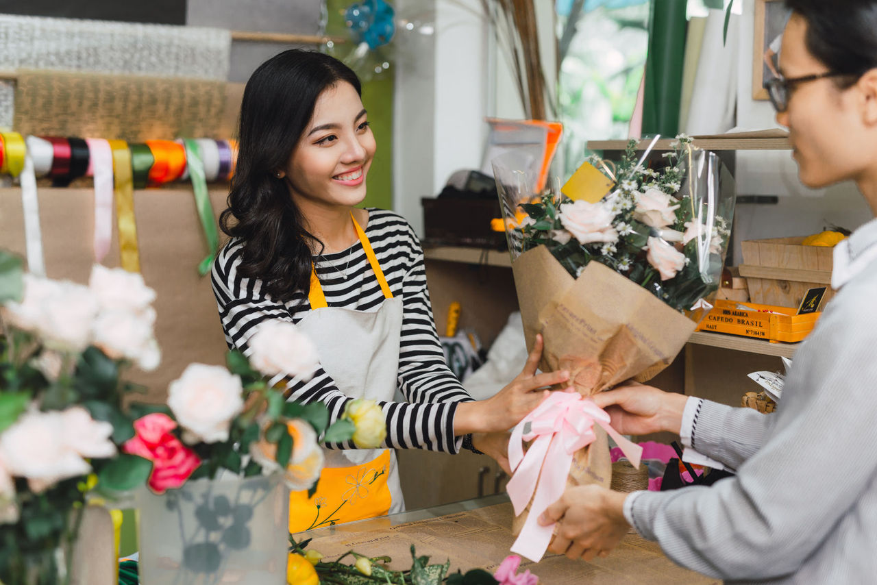 Ho Chi Minh City, Vietnam - 21 August, 2017: happy smiling florist woman making bouquet for and man or customer at flower shop